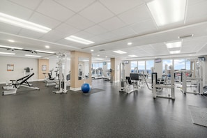 Une salle de sport spacieuse, équipée de divers appareils d’exercice, d’un ballon d’exercice bleu et de grandes fenêtres qui laissent entrer la lumière naturelle.