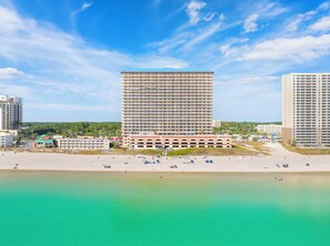 Un hotel de gran altura con varios pisos, una playa en primer plano y cielo despejado.