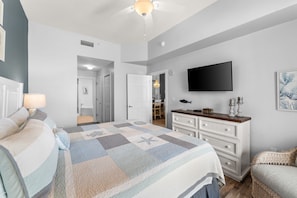 Une chambre à coucher comprenant un lit, une commode, un téléviseur et une porte donnant sur une salle de bain.