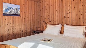 Et rum med træpaneler, en seng, puder, et natbord og et billede i ramme på væggen.