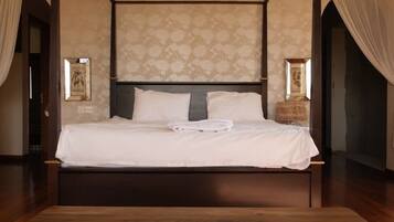 Una cama con dosel y estructura de madera, cabecera con estampado floral y un banco frente a la cama.
