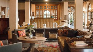 A spacious living area with a high ceiling, a ceiling fan, and a large window with a view. There are multiple seating areas, including a leather sofa and a round coffee table. - Little Daisy Manson |Two Villas | Sleeps 33 Jerome (Sedona)