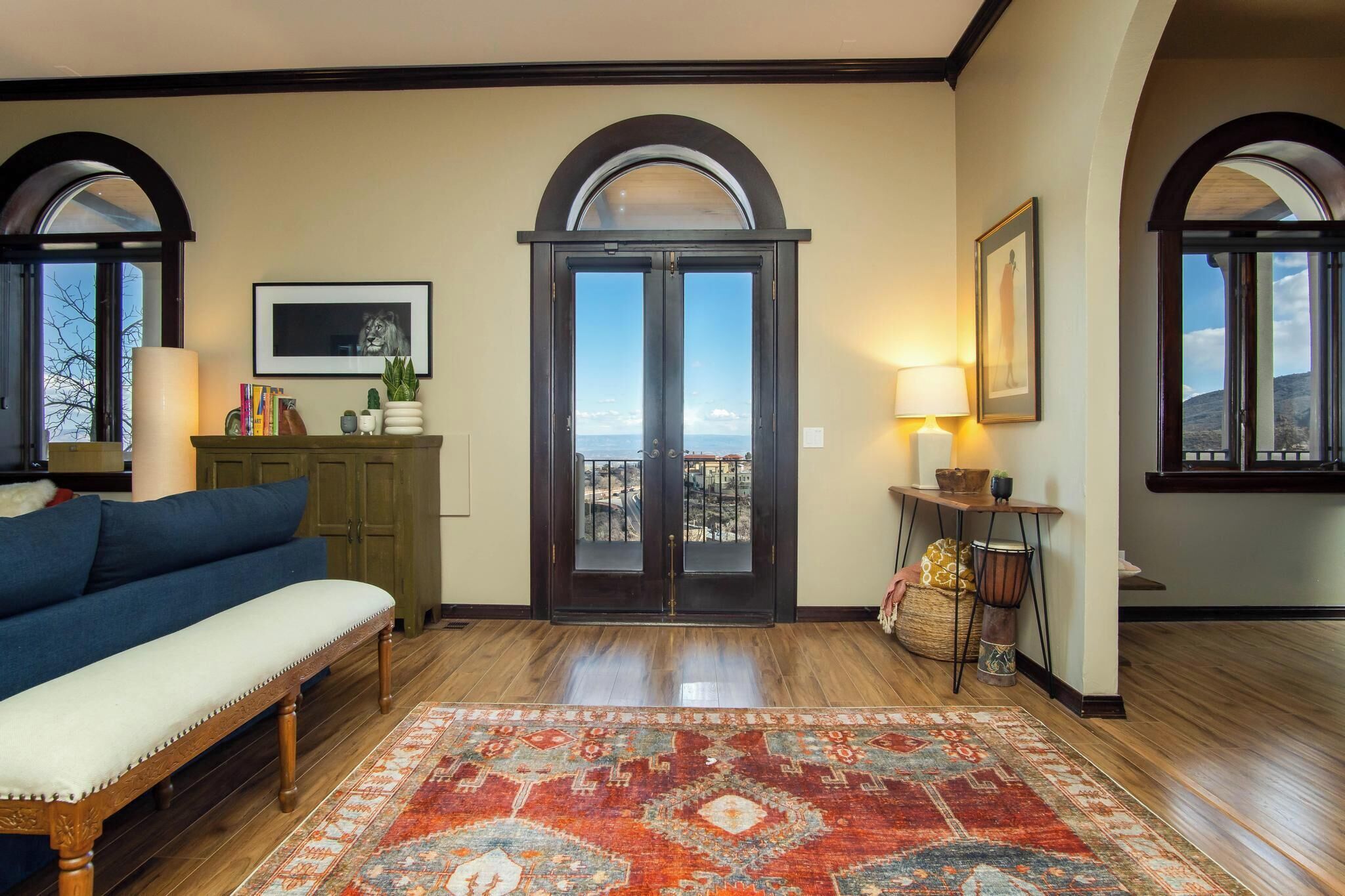 A spacious living room with a large bench, a colorful rug, and a view through a set of double doors.