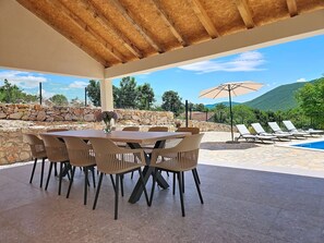 Eine Terrasse im Freien mit Tisch und Stühlen, ein Pool mit Liegestühlen und eine Steinmauer.