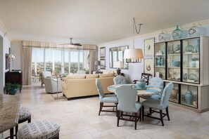 A spacious living room with a beige sofa, a dining table with chairs, and a decorative cabinet with glass doors. - Regatta - Walk to the Beach! (Naples)
