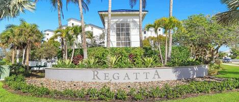 Un letrero con la palabra 'REGATTA' frente a un edificio de fachada blanca y una torre central, rodeado de palmeras y vegetación.