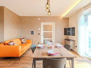 Ein modernes Wohnzimmer mit einem Holzespeisetisch, gedeckt für vier Personen, einer Couch und einem an der Wand befestigten Fernseher.