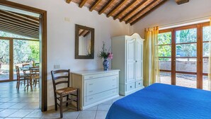 Ein Schlafzimmer mit Bett, Kommode, Stuhl, Spiegel und einem Fenster mit Blick ins Grüne.