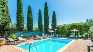 Ein rechteckiger Pool mit Fliesenränder, umgeben von Liegestühlen und Sonnenschirmen, mit Bäumen im Hintergrund.