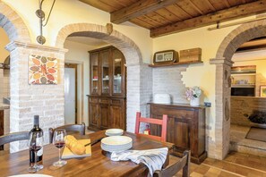 Zona pranzo rustica con camino in mattoni, pensili in legno e arco in pietra.