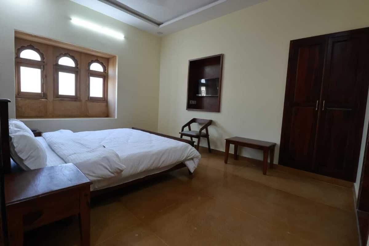 A bedroom with a bed, a wooden wardrobe, a small table, a chair, and a window with three panes.