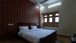 A bedroom with a bed, a window with arched design, and a striped wall. - Hotel Mahadev Residency Jaisalmer (Jaisalmer)