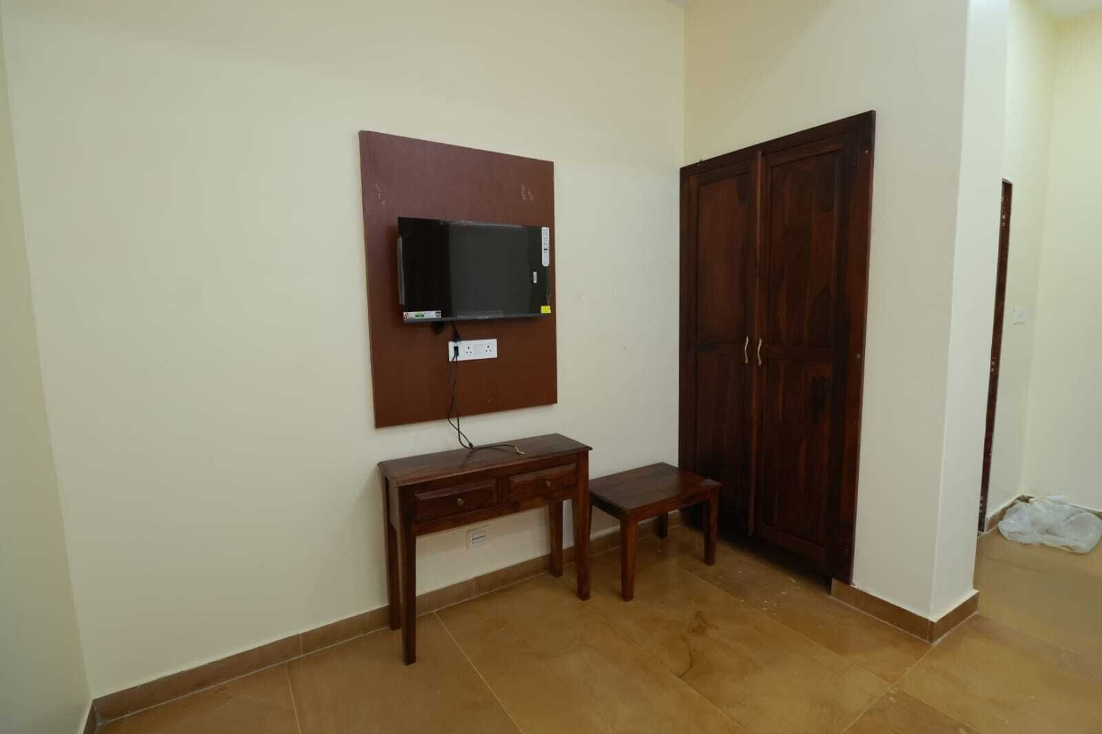 Ein Zimmer mit einem Holztisch, einem an der Wand befestigten Fernseher und einem Holzschrank.