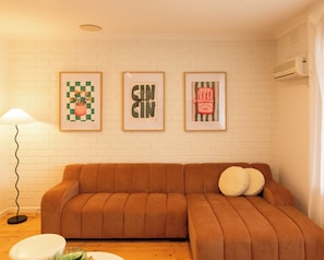 Un salon avec un canapé marron, une lampe et trois œuvres d’art encadrées accrochées au mur.