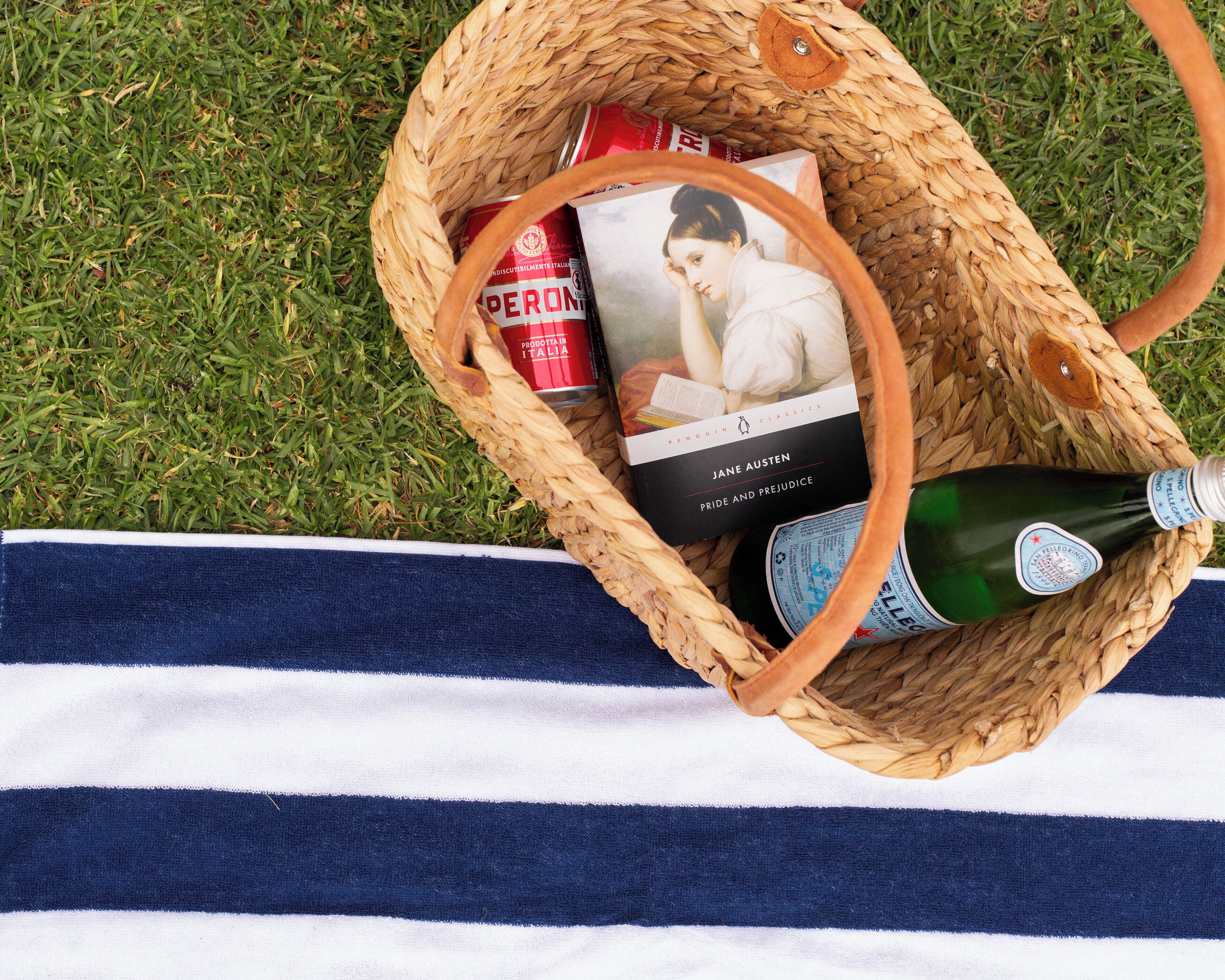 Una cesta de mimbre con un libro, una botella y una lata roja sobre una tela a rayas.