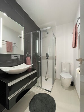 Ein modernes Badezimmer mit einer Duschkabine, einem weißen Waschbecken und einer Toilette.