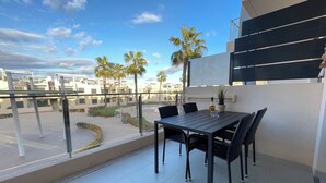 Un balcón con mesa y sillas, con vista a un patio con palmeras y edificios.