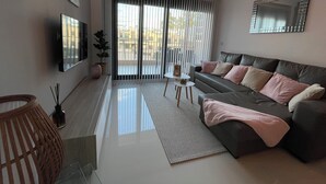 Una sala de estar moderna con un sofá, un televisor, una planta en maceta y un ventanal con persianas.