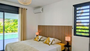 A bedroom with a bed, two bedside lamps, a window with blinds, and an air conditioning unit. - Villa Néréa - 4 Bedrooms and Pool - Near the Lagoon (Saint-Paul)