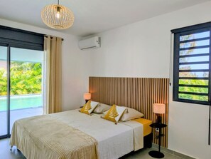 A bedroom with a bed, two bedside lamps, a window with blinds, and an air conditioning unit. - Villa Néréa - 4 Bedrooms and Pool - Near the Lagoon (Saint-Paul)