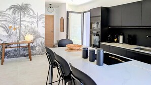 A modern kitchen with a black countertop, a dining area with a white table, and a mural of palm trees on the wall. - Villa Néréa - 4 Bedrooms and Pool - Near the Lagoon (Saint-Paul)