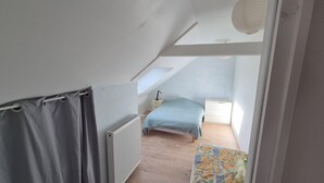 A narrow attic bedroom with a sloped ceiling, a radiator, a bed, a nightstand, and a window. - Cosy gîte upstairs (Sainte-Anne-sur-Vilaine)