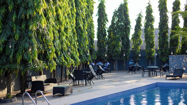 A swimming pool with lounge chairs and tables, surrounded by tall trees. - Lacasa Hotel Epe (Epe)