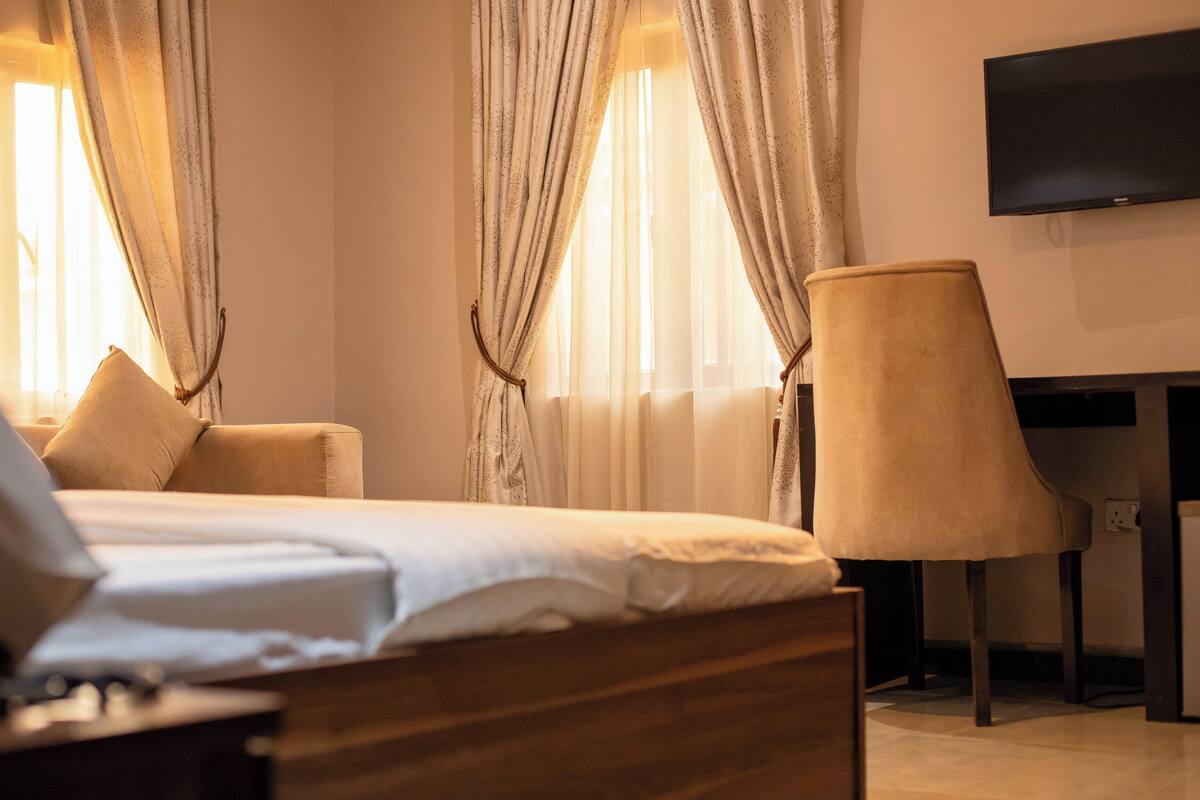 A hotel room with a bed, a chair, a TV, and curtains.
