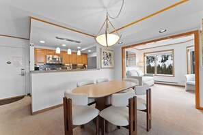 Eine moderne Küche mit Edelstahlgeräten, ein Essbereich mit Holztisch und -stühlen sowie große Fenster mit Blick ins Freie.