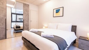 Ett modernt hotellrum med en stor säng, sängbord, en spegel och en inramad tavla på väggen.