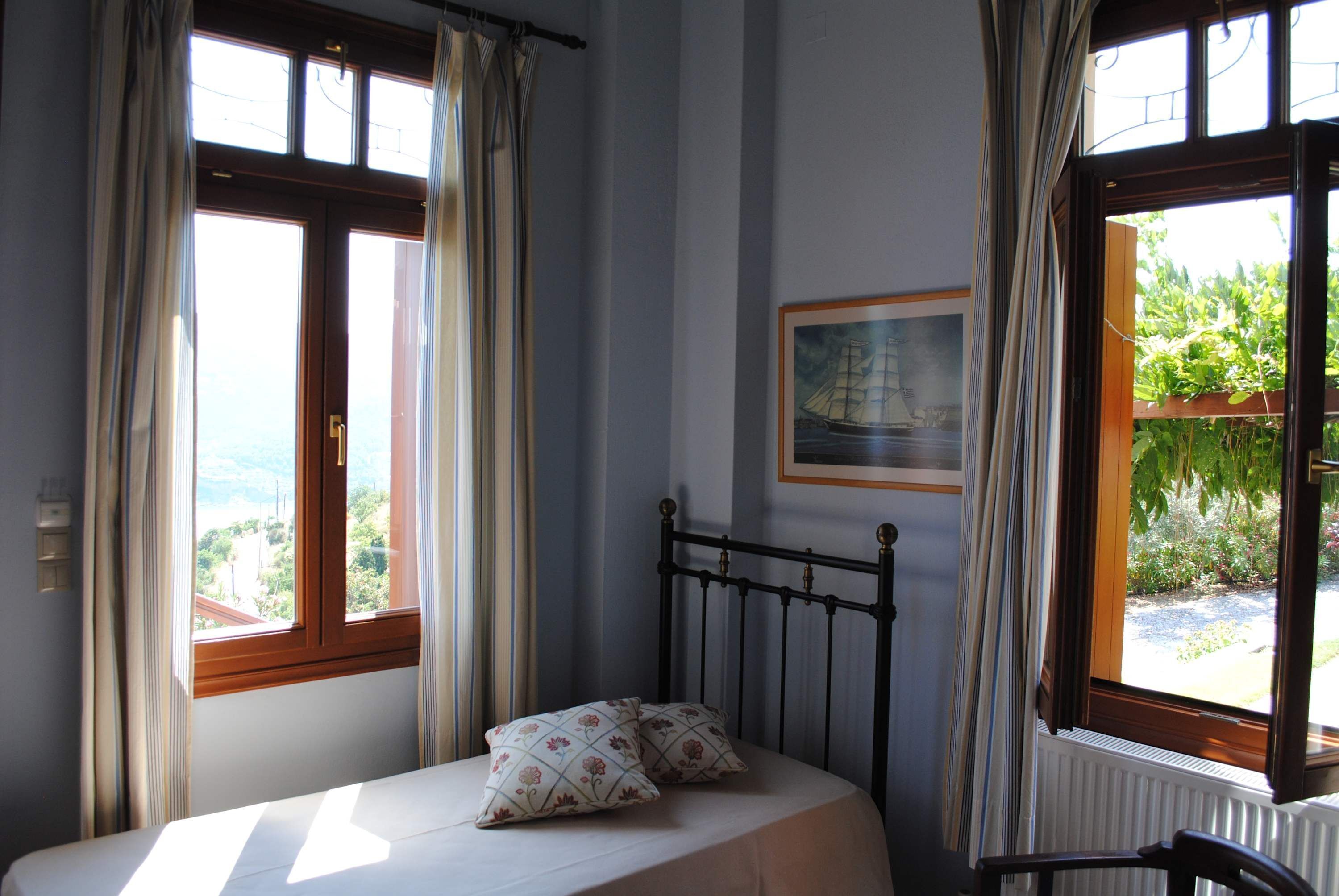 A bedroom with a bed, two windows, a radiator, and a framed picture on the wall.