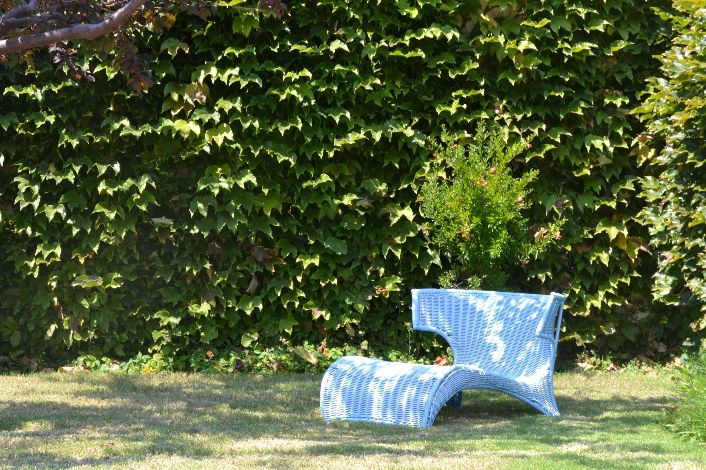 Une chaise en osier, placée dans un espace herbeux, avec une haie en arrière-plan.