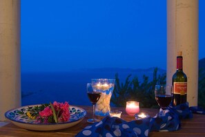 A table with a bottle of wine, a glass of red wine, a candle, and a bowl of flowers. - Stolios Skopelos - Erato Deluxe Panoramic View (Skopelos)