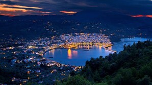 A coastal town at dusk with a prominent waterfront, dense residential area, and a central peninsula with illuminated buildings. - Stolios Skopelos - Terpsichore Split Level Nest (Skopelos)