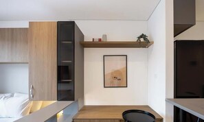 Ein modernes Zimmer mit einem Bett, einem Schreibtisch, einem Stuhl, einem Regal mit Dekoration und einem gerahmten Bild an der Wand.