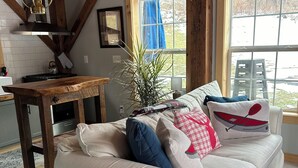 A cozy living room with a sofa, a wooden table, a potted plant, and a window with a view.