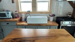 A kitchen with a wooden countertop, a sink, a microwave, and a stove.