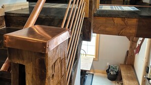 A wooden staircase with a metal handrail, a bunk bed, and a small seating area with a table and chair.