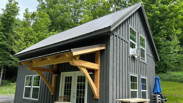 A wooden cabin with a porch, stone patio, and outdoor furniture.
