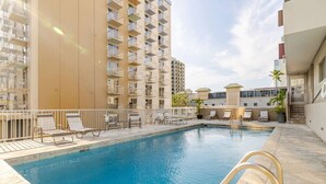 Una piscina con tumbonas y un edificio con balcones al fondo.