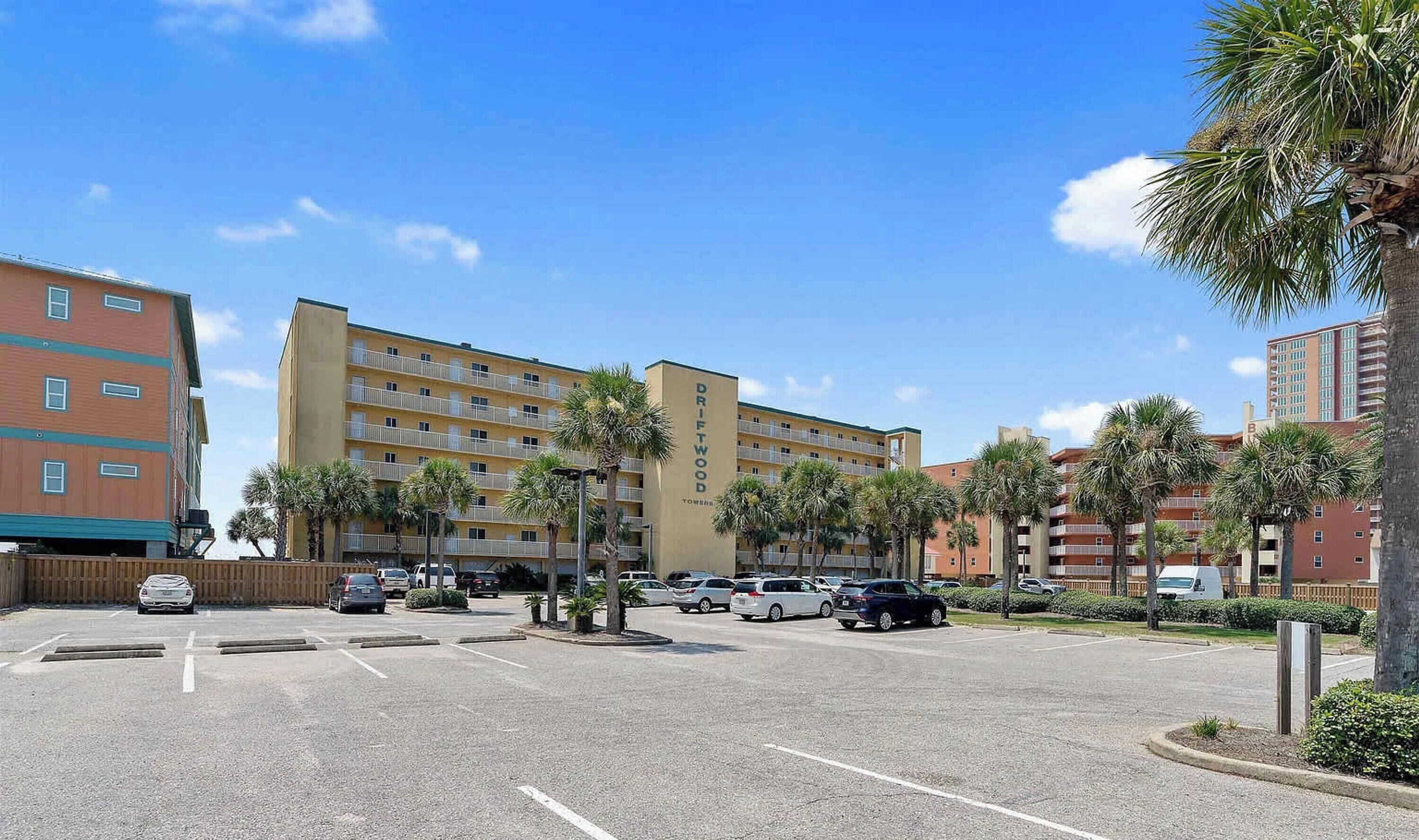 Un hôtel à plusieurs étages, doté d’un parking et bordé de palmiers.