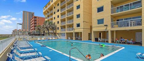A swimming pool with lounge chairs, a pool ladder, and a building with balconies in the background.