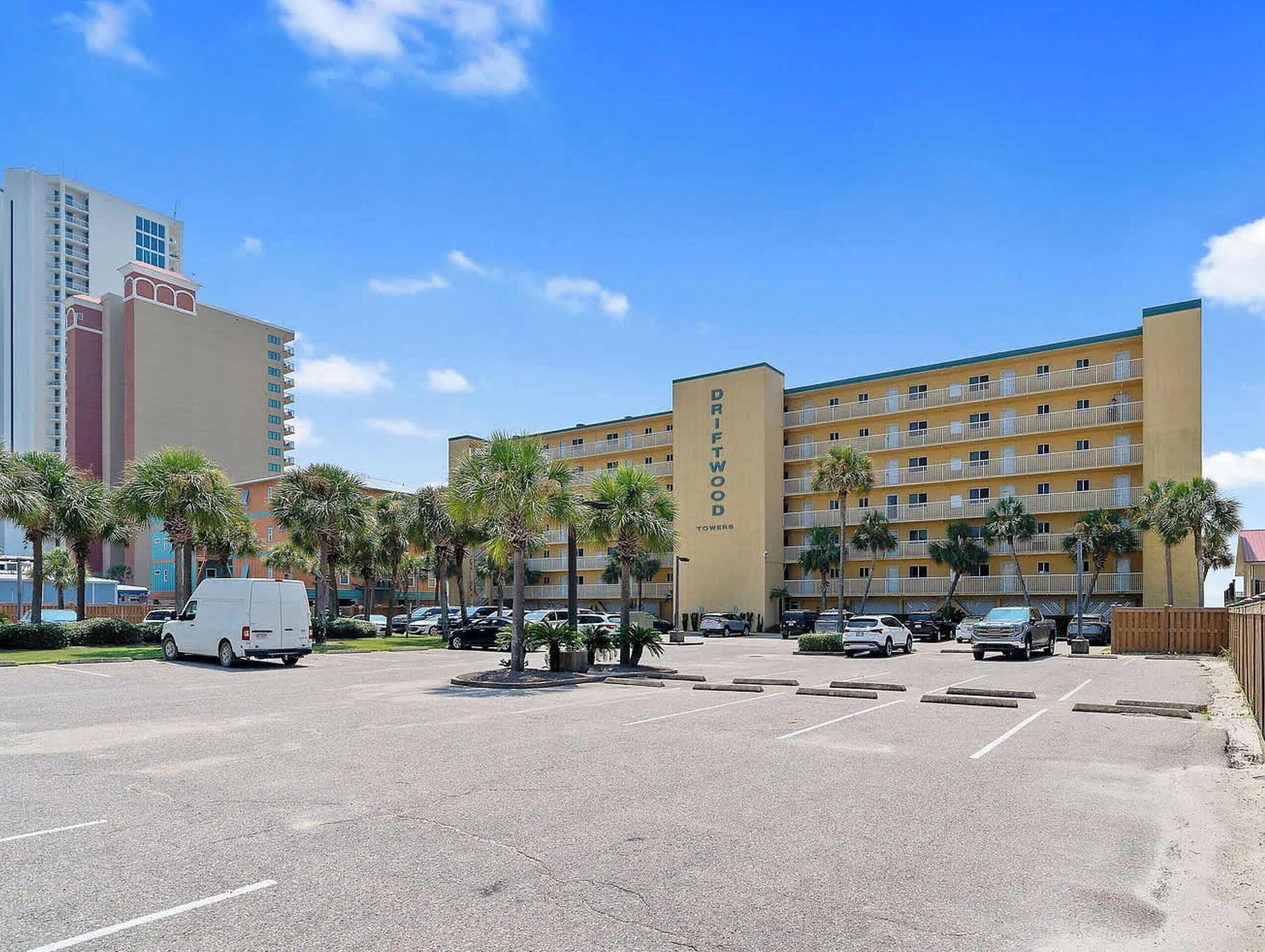 Een hotel met meerdere verdiepingen, een centraal binnenterrein, parkeerplaats en palmbomen.