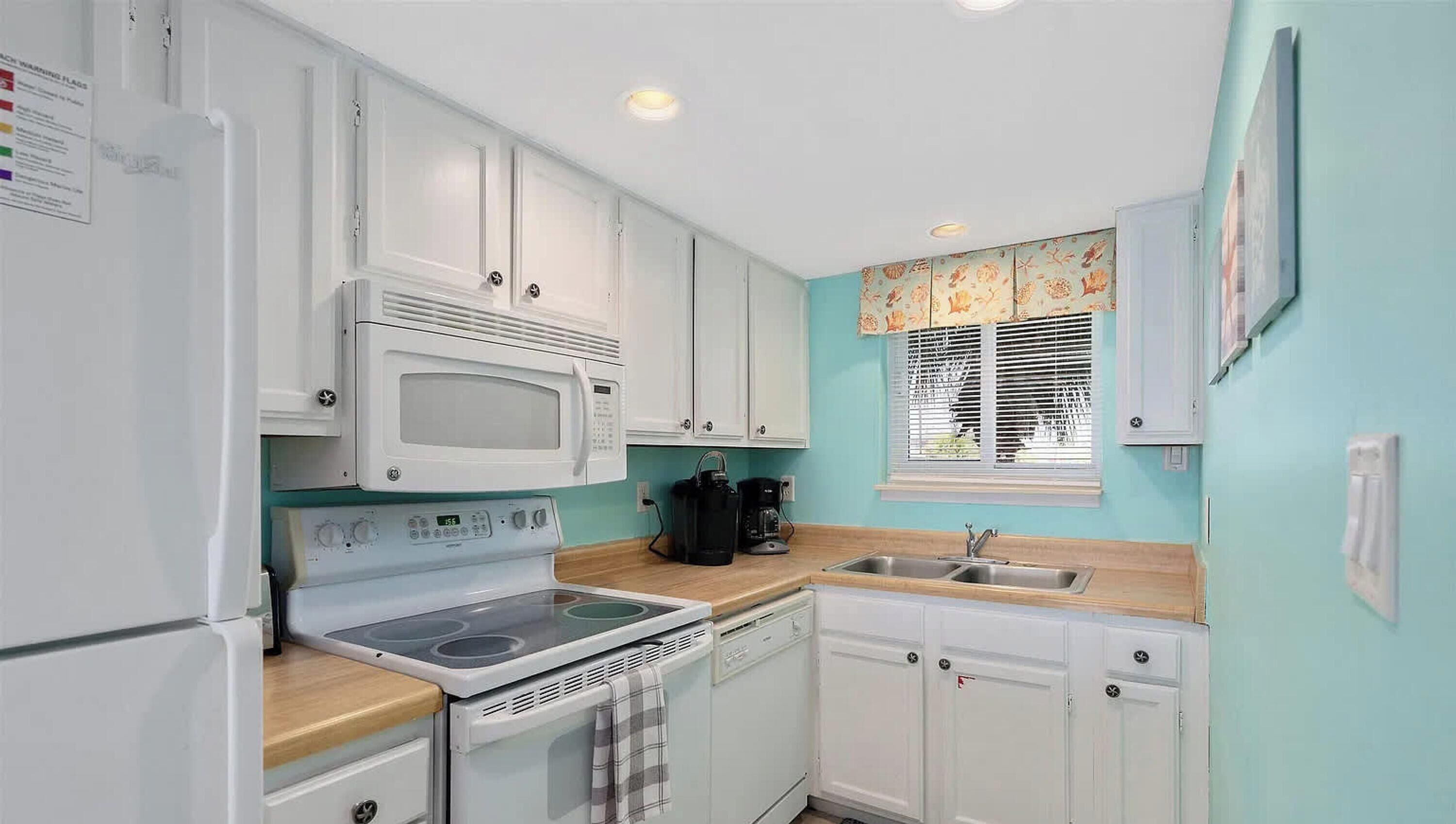 A compact kitchen with white cabinets, a microwave, stove, and a sink.