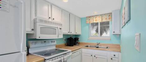 A compact kitchen with white cabinets, a microwave, stove, and a sink.