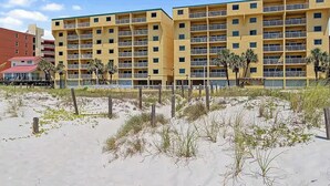 A multi-story hotel with balconies, located near a sandy beach with sparse vegetation. - The Big Surf II - Gulf View - Beach Pool and Fun (Gulf Shores)