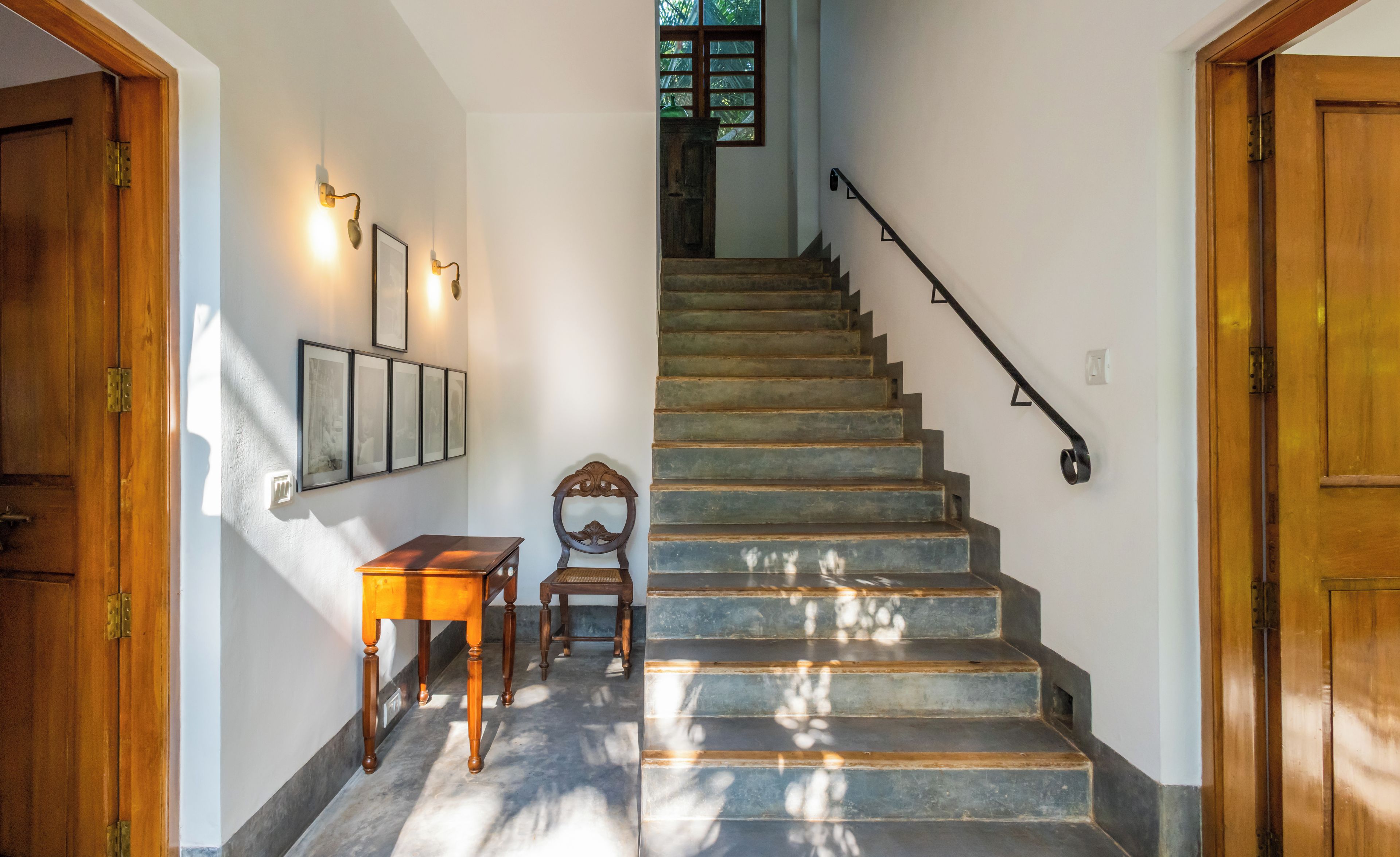 Una escalera con barandilla, una mesa de madera y luces fijadas a la pared.