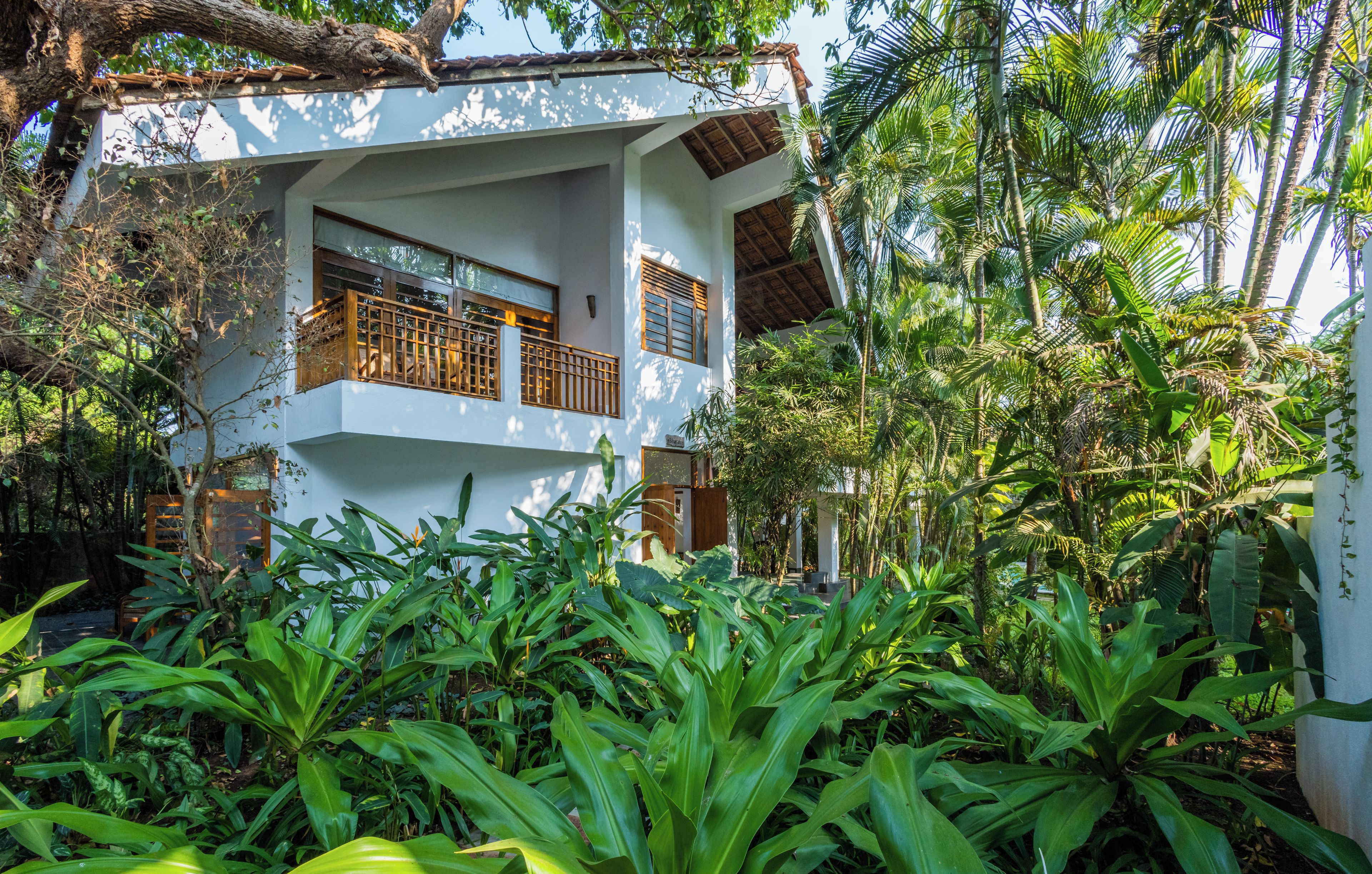 Un edificio de dos plantas con un balcón, rodeado de exuberante vegetación tropical.