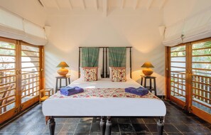 Una habitación con cama, dos mesitas de noche, una ventana con cortinas y una puerta con vistas.