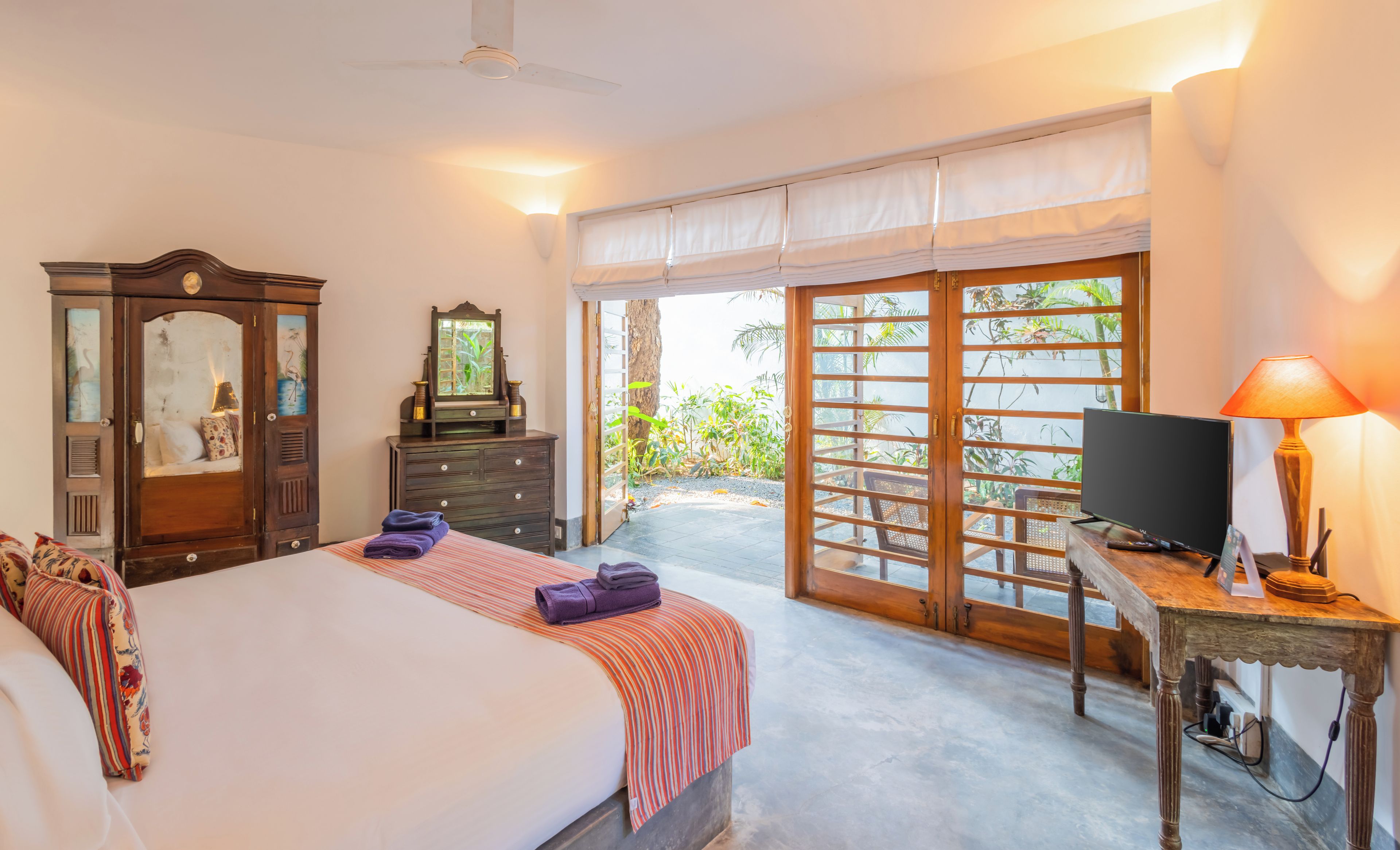 A bedroom with a bed, dresser, mirror, television, and a view through a sliding door.